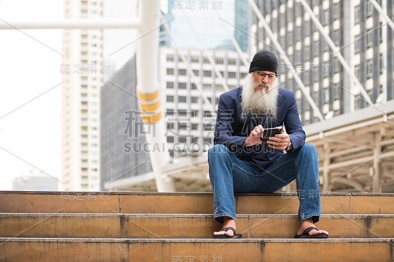 长着胡子的成熟商人坐在户外的城市里打电话