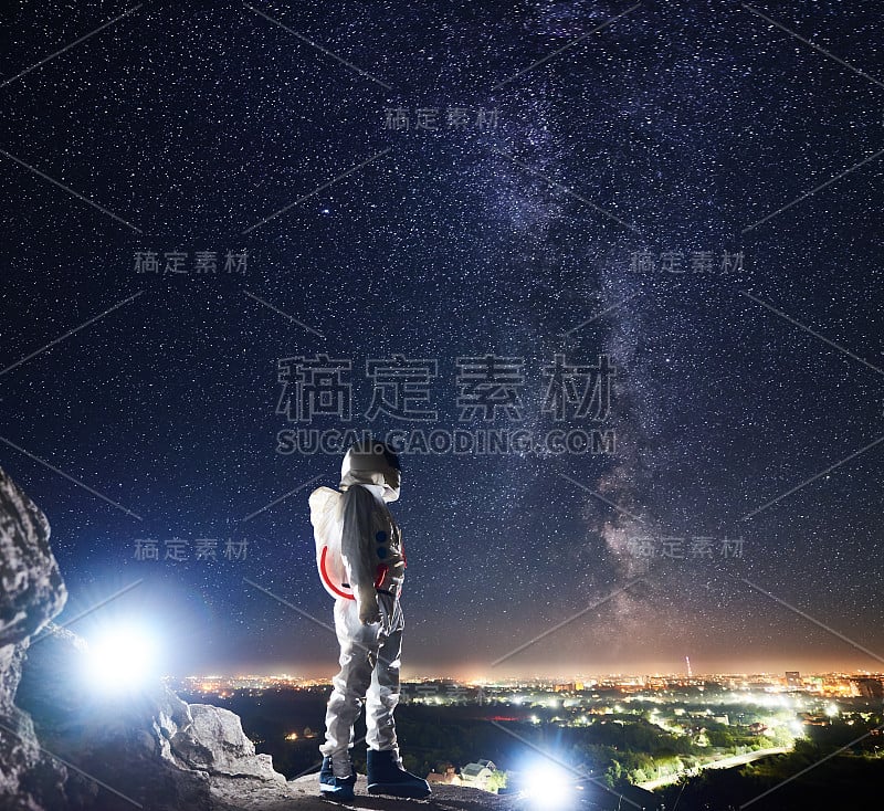 宇航员站在布满星星的夜空下的岩石山上。