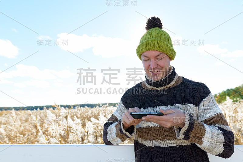 年轻快乐的男人微笑着，用手机对着风景的秋天芦苇田