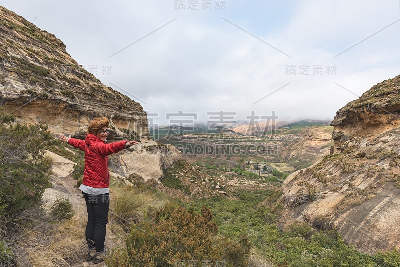 游客伸开双臂站在雄伟的金门高地国家公园，欣赏南非的旅游目的地的全景。冒险家的概念和旅行的人。