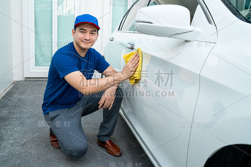 车饰上，一名身穿蓝色制服的男子清洗着一辆白色轿车，手里拿着一辆超细纤维洗车大车。