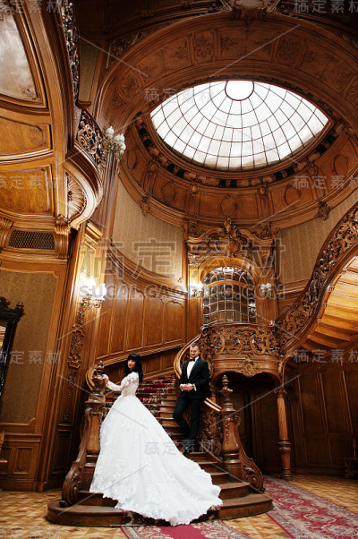 一对神奇的新婚夫妇在富丽的宫殿的大木楼梯上。