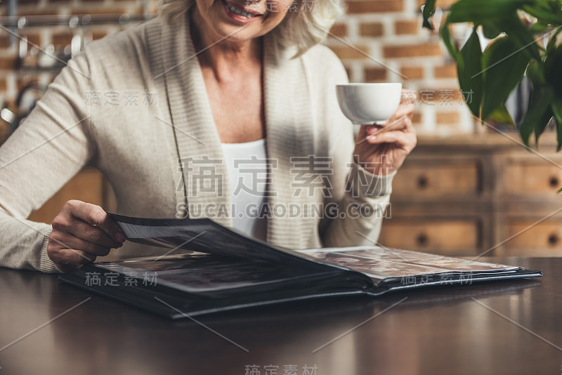 高级妇女坐在厨房桌子旁看相册的肖像