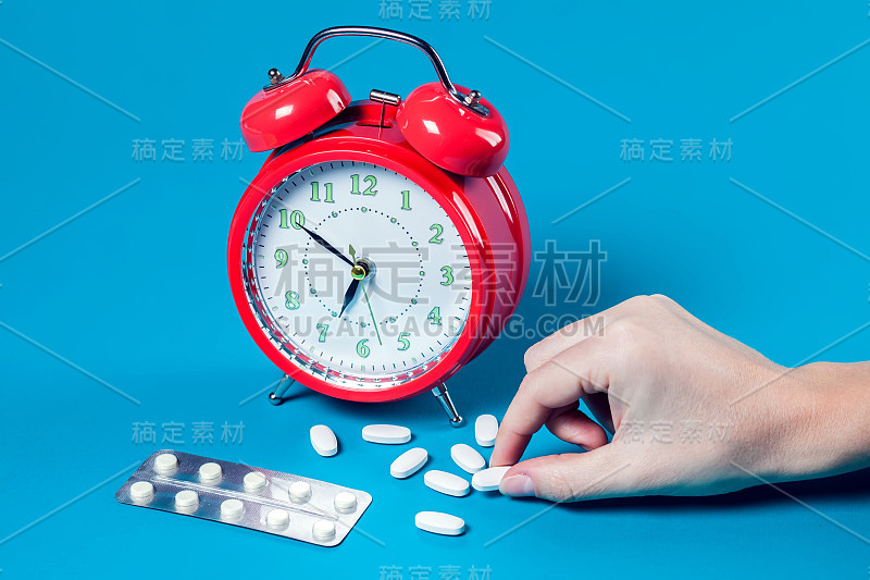闹钟，彩色背景上的药丸。正在吃药的女人的手。医疗保健理念