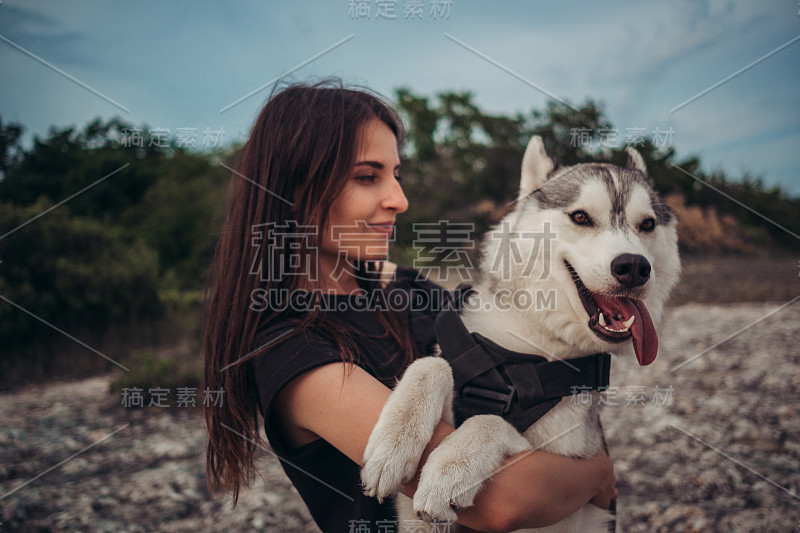 日落时分，美丽的女孩和一只灰白相间的哈士奇在山里玩耍