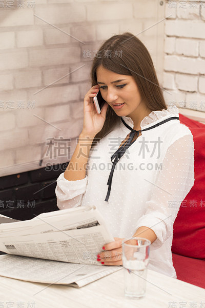 一名年轻女子在看报纸广告和通过手机寻找出租公寓