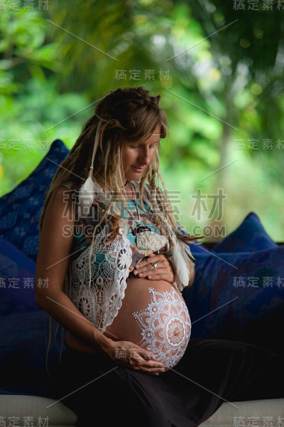 一个梳着波西米亚长发绺的白人孕妇。白色的迈赫迪在大肚子。对婴儿在新时代生活方式的期望。