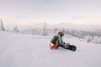 坐着的女性滑雪板戴着长头发准备从山顶骑