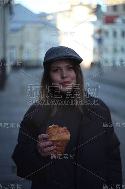 年轻漂亮的女孩在街上吃牛角面包